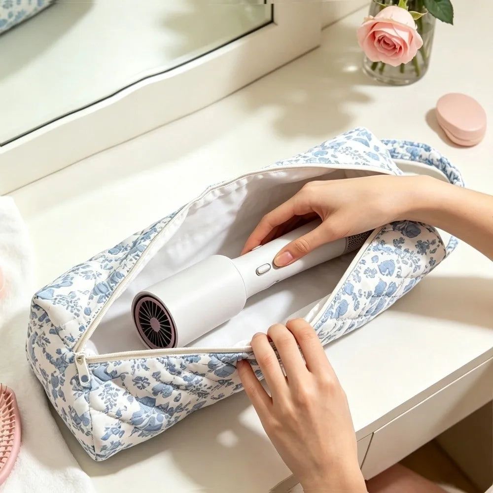 A hand is opening a quilted cotton hair dryer storage bag with a handle, revealing a white hair dryer inside.