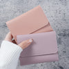 A hand holds a pink slim triple-fold PU leather wallet with a white knitted sleeve in a gray background.