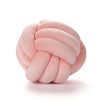 A soft pink handmade knitted and knotted velvet throw pillow with a round, textured design.