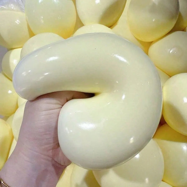 A hand is holding a smooth, pale yellow slow-rebound stress relief ball surrounded by many similar balls.