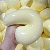 Eine Hand drückt einen großen, glatten, blassgelben Stressball aus, umgeben von vielen ähnlichen Bällen.