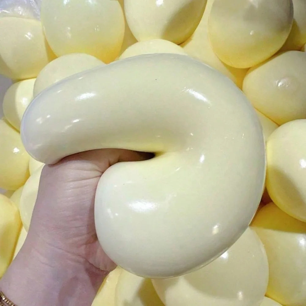 Eine Hand drückt einen großen, glatten, blassgelben Stressball-Fidget-Ball, umgeben von vielen ähnlichen Bällen.