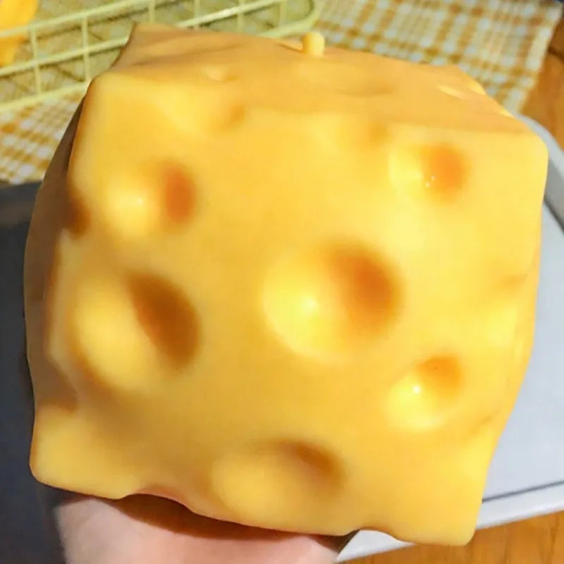 A large, yellow, cube-shaped cheese fidget toy with dimples is held in a hand.