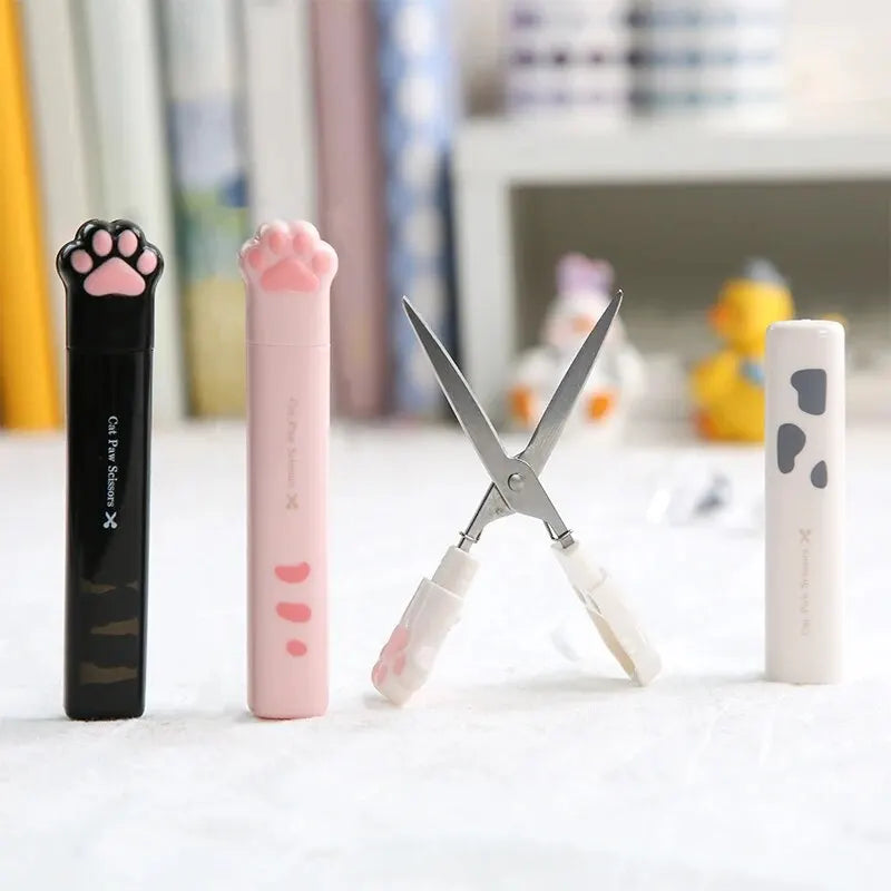 A set of stainless steel cat paw portable scissors in black and pink are displayed on a white surface.