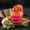 Jar of bright red hot sauce with a pink label and fresh basil leaves on a wooden board.