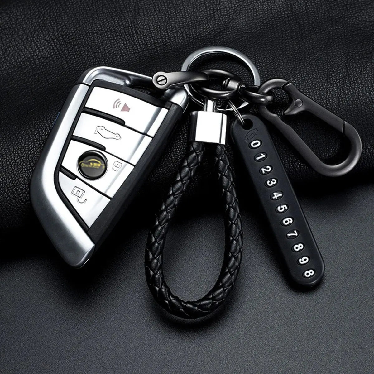 A silver personalized phone number keychain with a braided black leather rope and metal clasp.