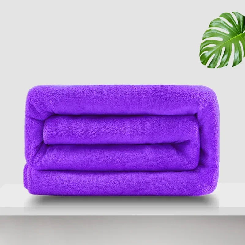 A stack of three vibrant purple ultra-soft microfiber bath towels on a white shelf.