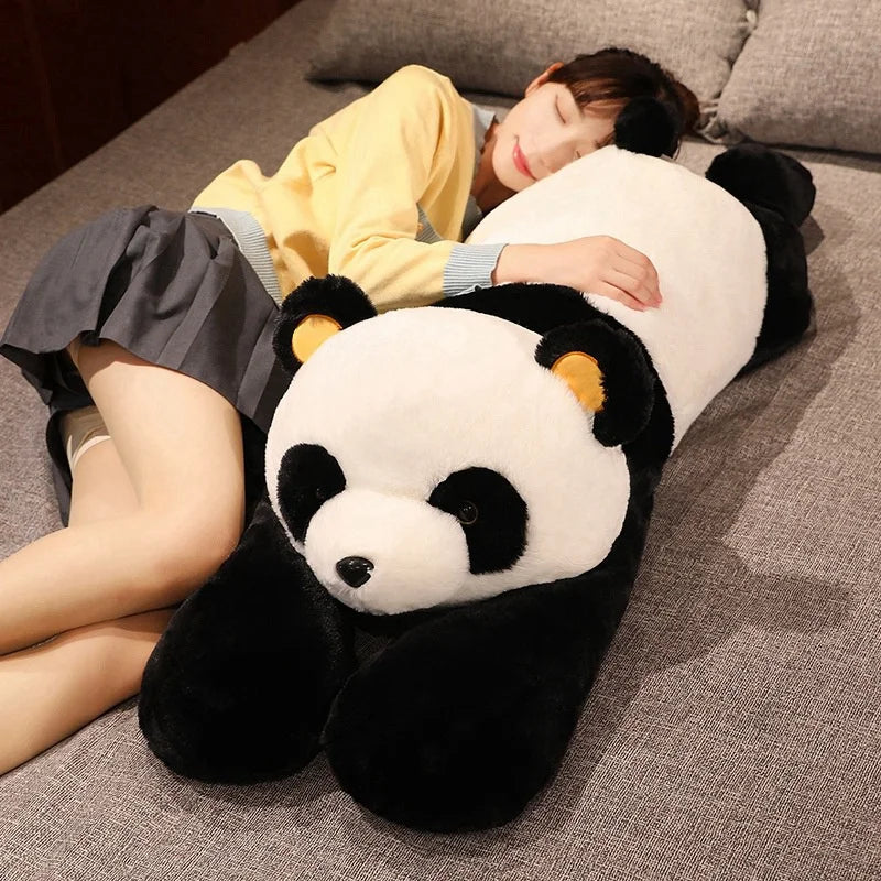 A person is relaxing on a couch with a giant soft panda plush toy, which has long arms, resting beside them.