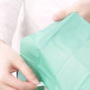 A hand is holding a folded light green disposable toilet seat cover.