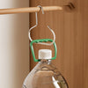 A green and white hanger hook system is shown hanging from a wooden rod against a light brown wall.