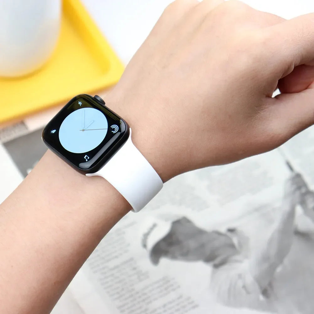 A hand is wearing a white silicone sport band on an Apple Watch, with a yellow object in the background.