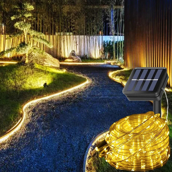 A coil of warm yellow LED string lights is placed on a gravel path in a garden setting.