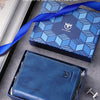 A blue leather bifold wallet is displayed in its box alongside a pen and keys.