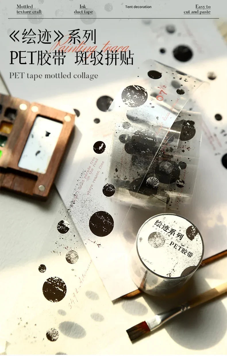 A roll of decorative PET tape featuring a mottled collage design, shown next to a brush and paper.