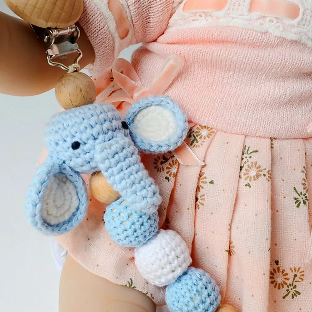 A wooden pacifier clip with crochet beads hanging from a chain, worn by a baby in a pink outfit.