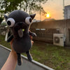 A gray plush chihuahua dog keychain pendant is held up against a sunset backdrop.