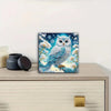 A square painting featuring a detailed owl with blue and white feathers set against a starry night sky and fluffy clouds.
