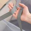 A hand is holding a gray fabric handle of a folding mesh laundry basket.