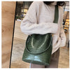 A woman wearing a beige sweater holds a dark green alligator pattern crossbody bag.