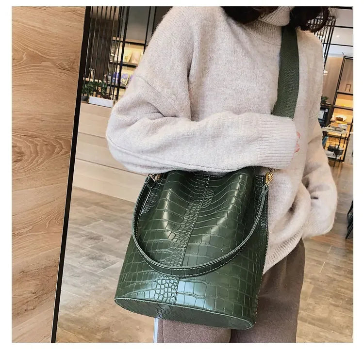 A woman wearing a beige sweater holds a dark green alligator pattern crossbody bag.