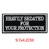 Black embroidered iron-on letter patch with white text reading HEAVILY SEDATED FOR YOUR PROTECTION
