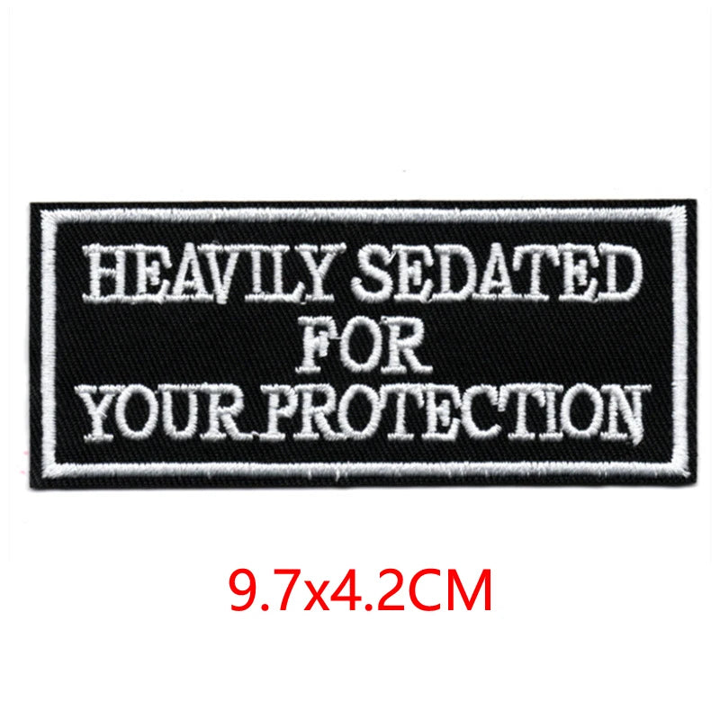 Black embroidered iron-on letter patch with white text reading HEAVILY SEDATED FOR YOUR PROTECTION