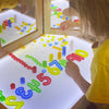 A child is using a transparent number counting set to form numbers and shapes on a light-up board.