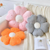 A collection of plush daisy flower throw pillows in pink, gray, and orange resting on a cream knitted blanket.