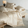A luxurious beige mulberry silk duvet cover set displayed on a bed with matching pillows and a bedside lamp.