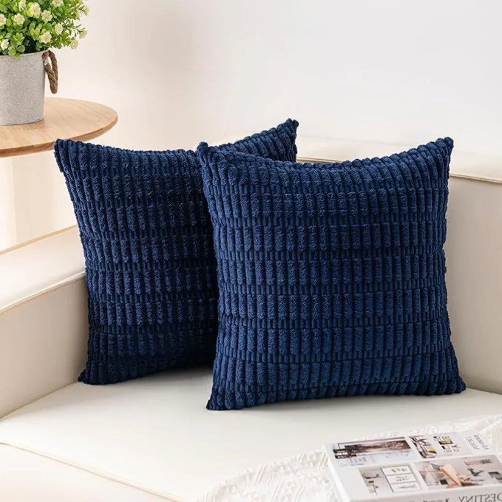 Two dark blue corduroy pillows with a striped velvet design resting on a white surface.