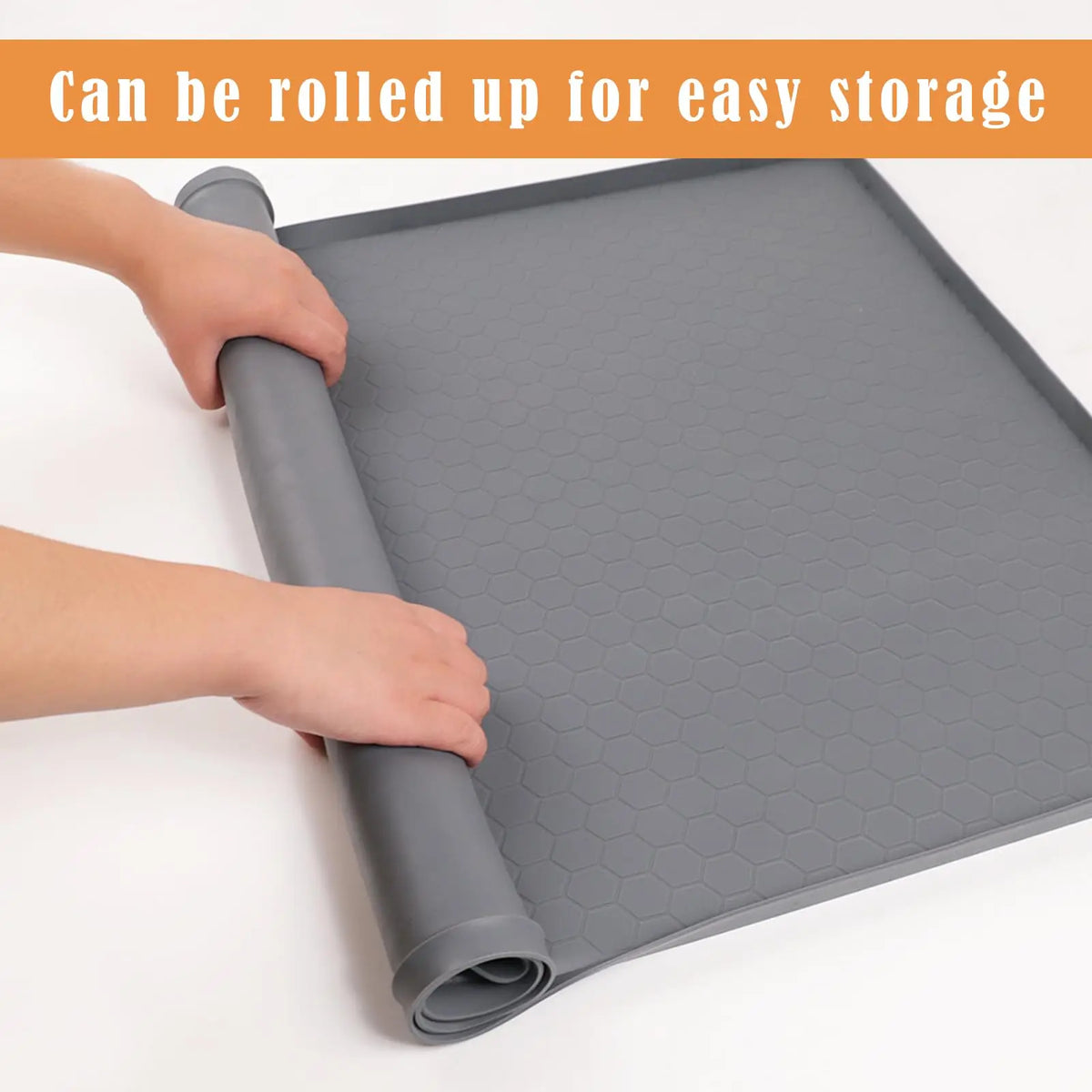 A hand is rolling up a gray silicone under sink mat to demonstrate its easy storage.