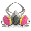 A gray full-face respirator mask with pink filters and adjustable straps is shown on a white background.