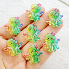 A hand holds several bright green and yellow resin charms shaped like sea creatures for crafting