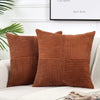 A set of two brown corduroy patchwork throw pillows with vertical ribbed texture displayed on a white sofa.