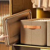 A brown fabric storage box is being pulled out from a wooden drawer, showing its textured surface and metallic trim.