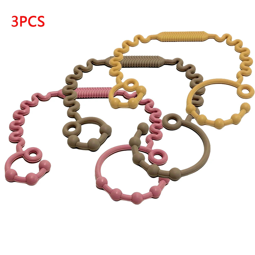 Three silicone pacifier clips or teethers in various colors including pink, beige, and gray.