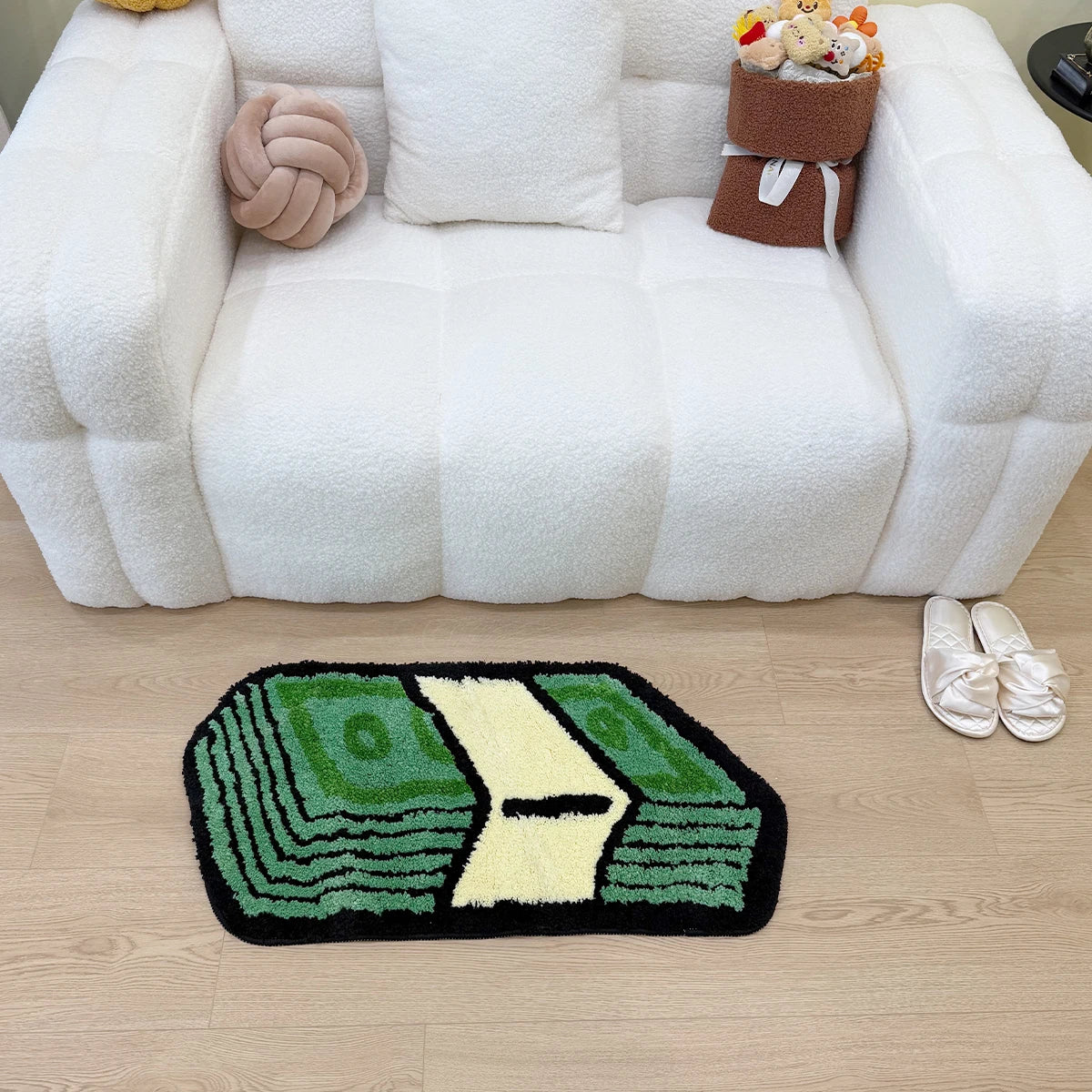 A green and yellow cartoon dollar bill mat is placed on a light wood floor in front of a white tufted sofa.