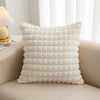 A white, quilted plush decorative pillow cover resting on a light-colored sofa.
