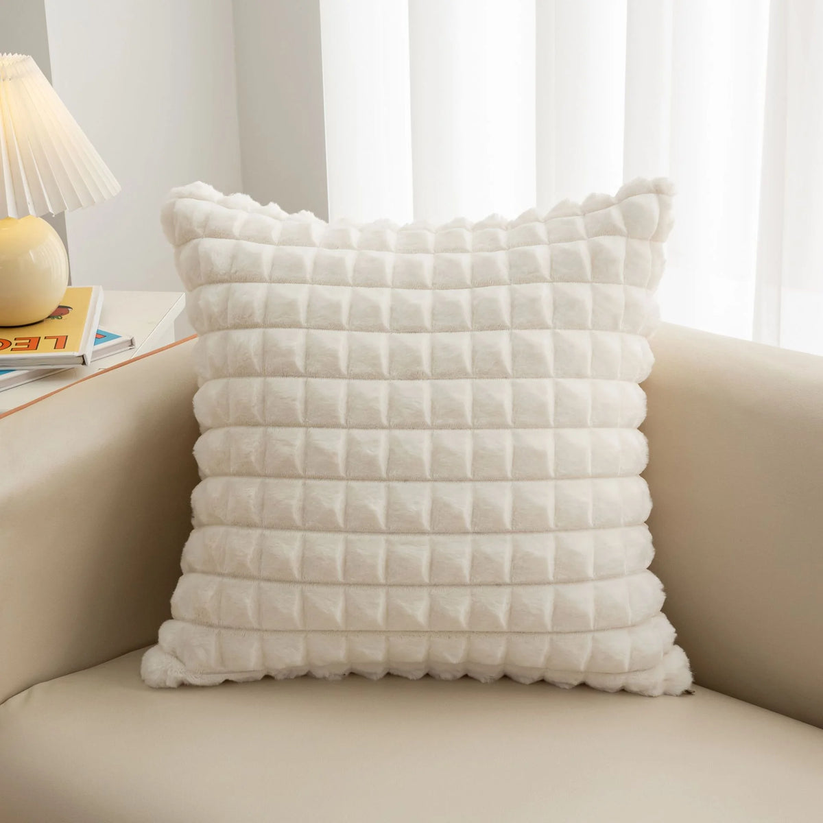 A white, quilted plush decorative pillow cover resting on a light-colored sofa.