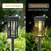 A black solar path light fixture with a warm glow is shown outdoors in a garden setting.