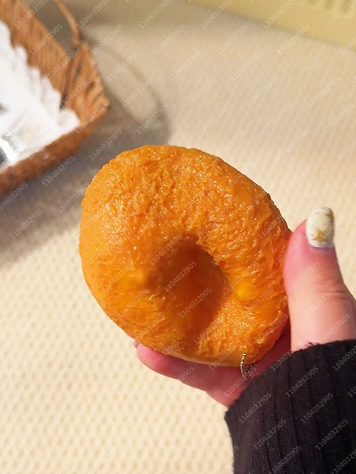 Eine Hand hält einen leuchtend orangefarbenen, strukturierten Knall-Kartoffel-Stressball als Spielzeug vor einem hellen Hinte