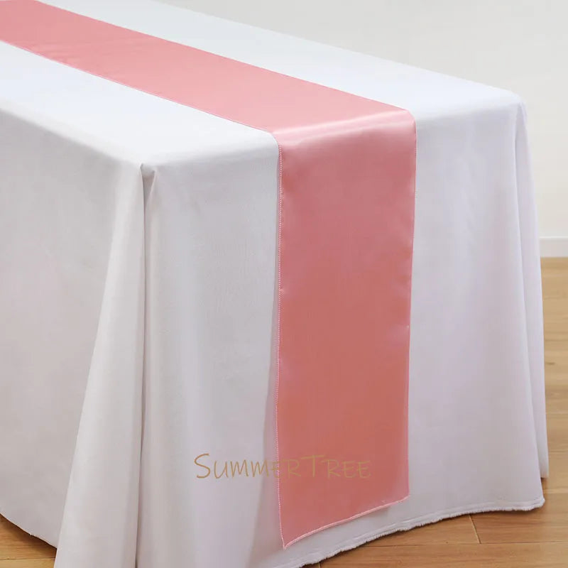 Elegant satin table runner in peach color draped across a white tablecloth.
