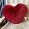 A deep red, fluffy heart-shaped plush throw pillow resting on a light beige surface.