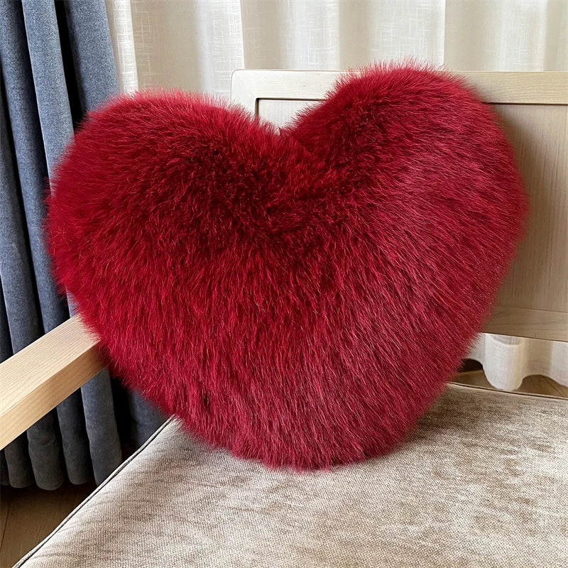 A deep red, fluffy heart-shaped plush throw pillow resting on a light beige surface.