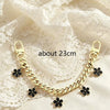 A gold-colored chain necklace with black flower charms displayed on a white lace fabric.