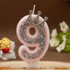 A pink rhinestone crown number candle shaped like the number 9 on a white base.