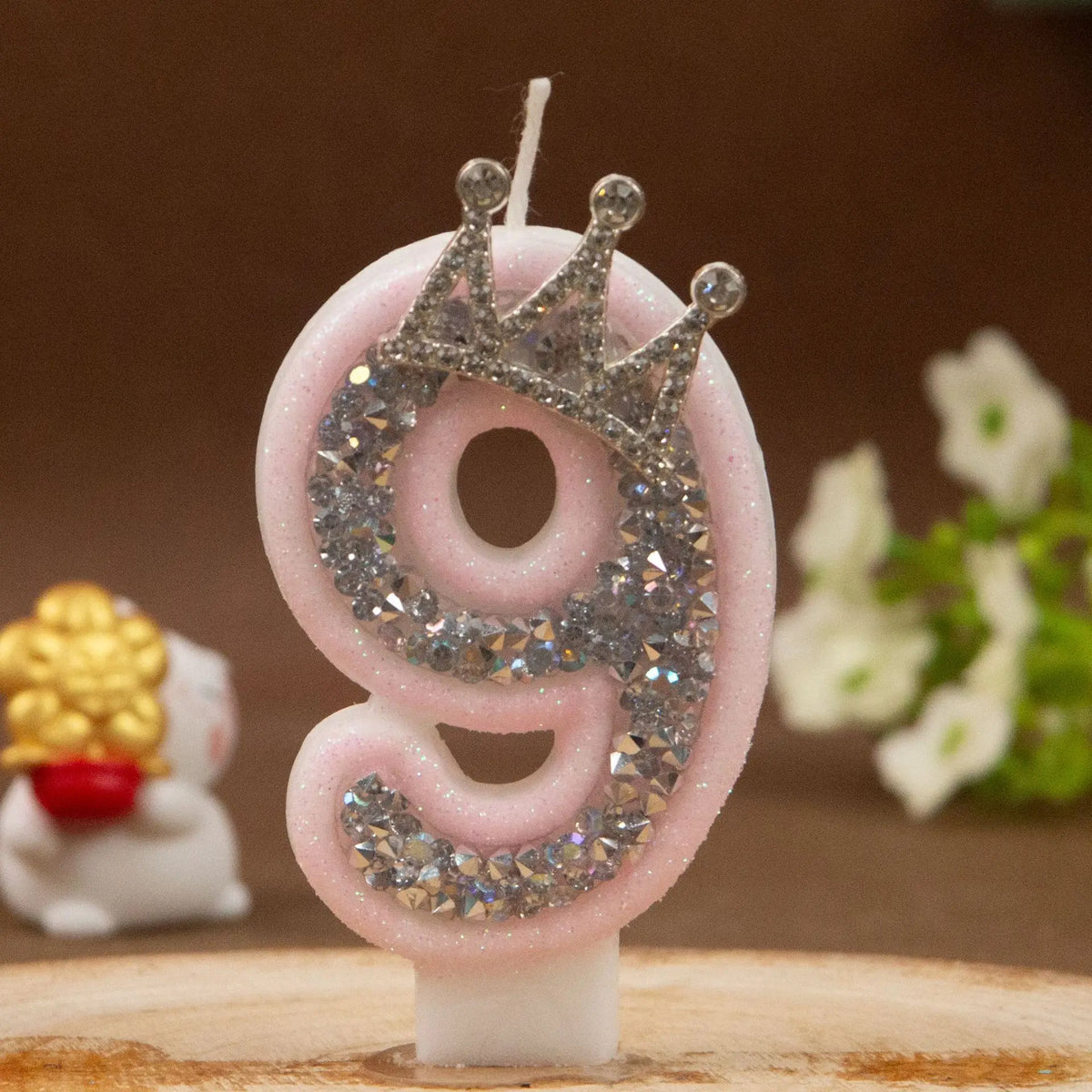 A pink rhinestone crown number candle shaped like the number 9 on a white base.