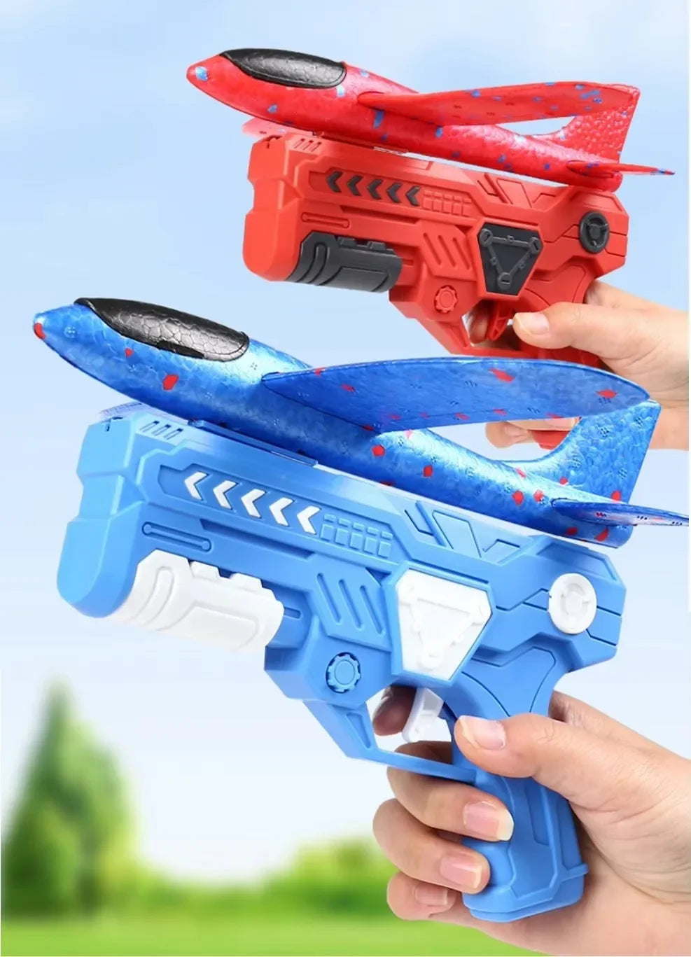 Two foam glider plane launchers, one red and one blue, are held by hands against a blurred green background.