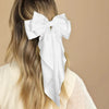 A woman's blonde hair is styled with a white silk bow hair clip and ponytail holder.