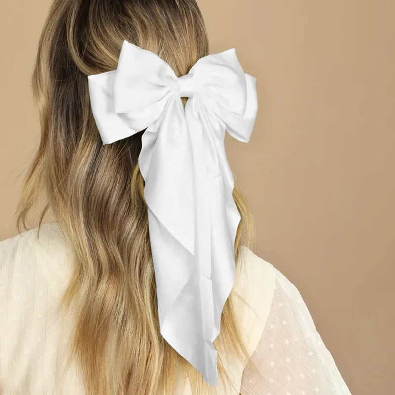 A woman's blonde hair is styled with a white silk bow hair clip and ponytail holder.